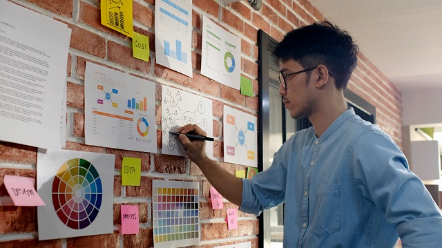 Image of young Asia man standing in front of a board of ideas