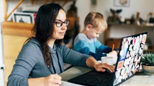 Image of woman working from home on a laptop with child next to her