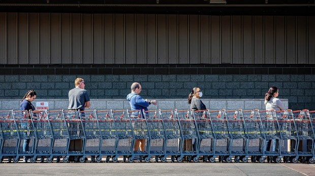 Five people waiting outside a supermarket, standing far apart.