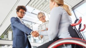 Young businessman greets colleague in wheelchair with handshake in the company