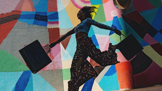 Image of woman jumping with shopping bags against colourful mural.