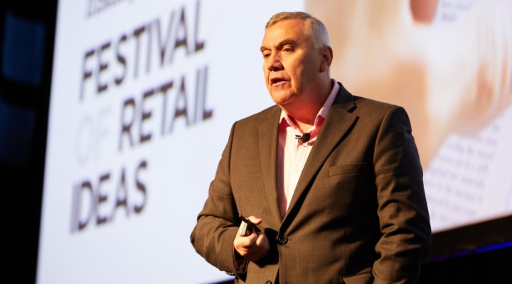 Bernie Brookes on stage at Retail Week in front of a big screen.