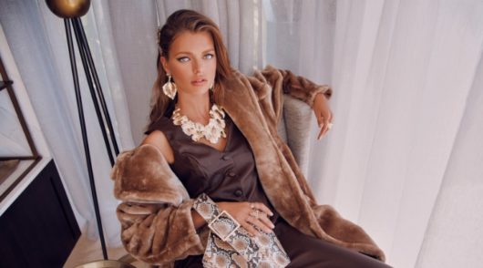 Girl with long hair and lots of jewellery on a chair with a faux fur coat.