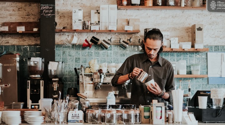 A barista with a man bun pouring coffee.