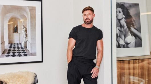Ikkari founder Adrian Norris stands in a beautifully designed home wearing black pants and t-shirt.