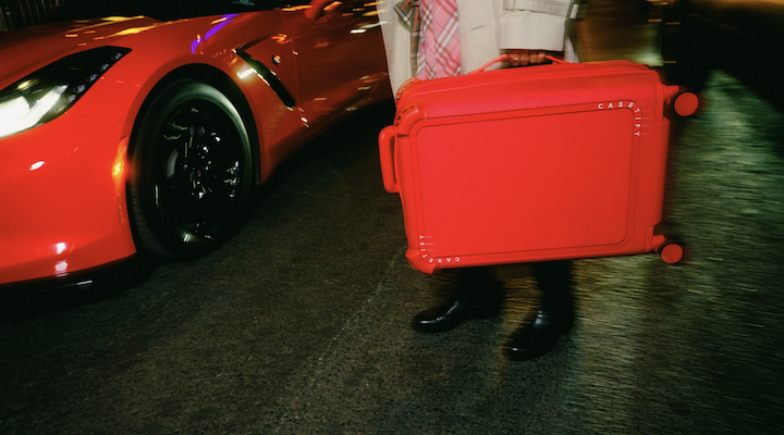 A person carrying a bright-red suitcase from Casetify’s Travel Bounce collection.