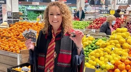 Lisa Ronson stands in front of the produce section in a Coles supermarket holding products in her hands.