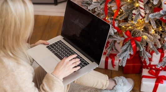 Happy young woman working on laptop in front of Christmas tree.