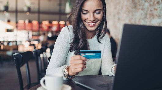 Smiling businesswoman holding a credit card and using laptop in a restaurant